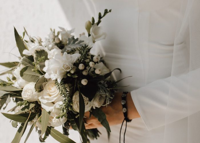 Minimalistic wedding dress for the bride and beautiful wedding bouquet made of white flowers and greenery, classy attire